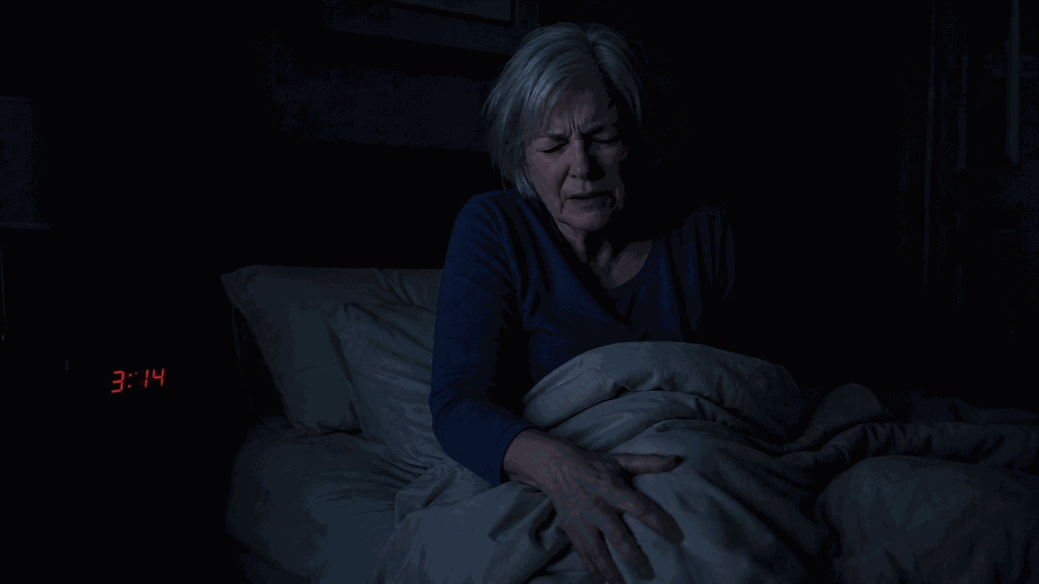 A woman awake in bed at 3:14 a.m., hand on her knee