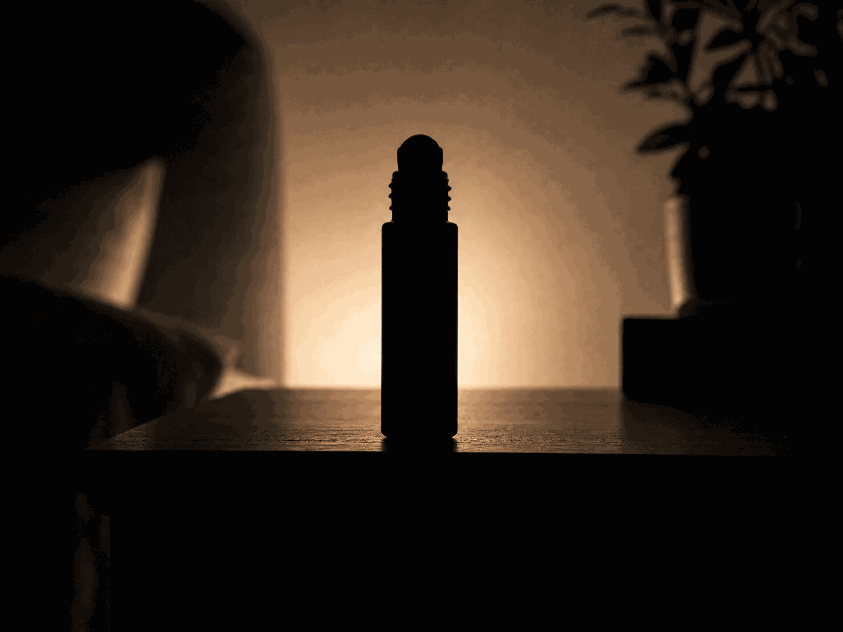 A small roll-on bottle in silhouette on a nightstand